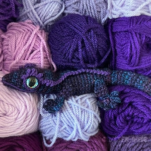 crocheted purple crested gecko sitting among purple yarn