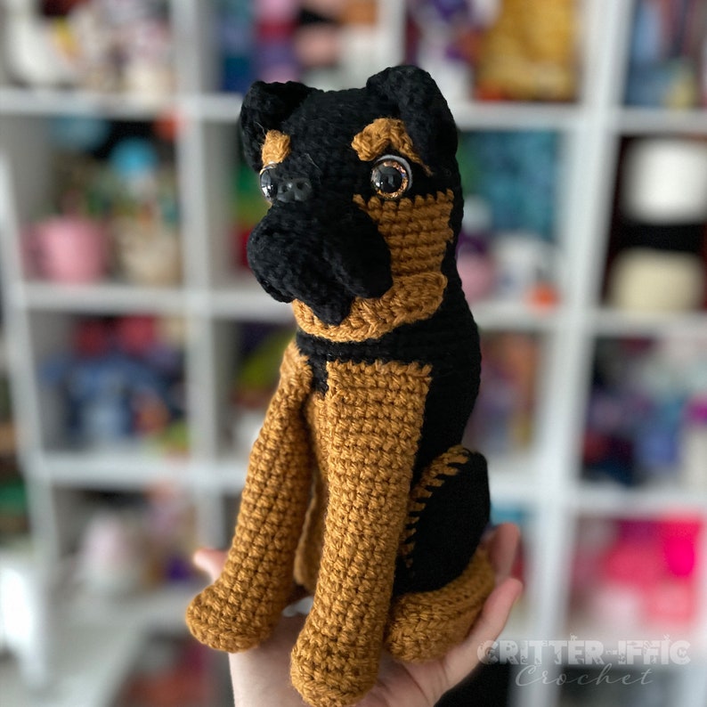 Crocheted brussels griffon dog sitting on a hand in front of a blurred background