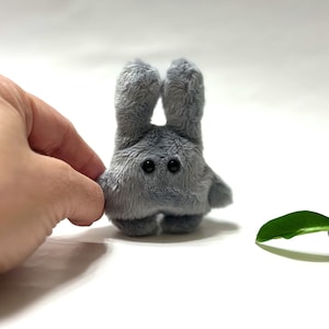 May include: A small gray plush bunny with large black eyes. The bunny is standing on a white surface.