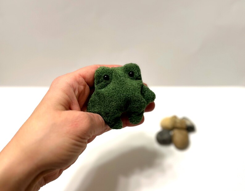 K&ouml;nnte beinhalten: Ein kleiner gr&uuml;ner Pl&uuml;schfrosch mit schwarzen Augen. Der Frosch sitzt in einer Hand.