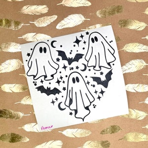 May include: A white sticker with three black ghosts, bats, stars, and crescent moons. The ghosts are arranged in a heart shape. The sticker says "Remark" in pink.