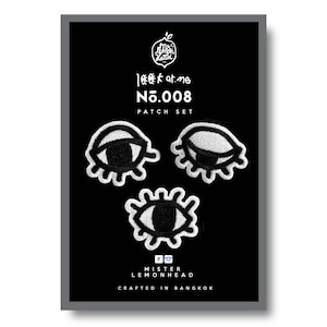 Può includere: Un set di tre toppe ricamate in bianco e nero con occhi stilizzati. Le toppe sono etichettate "look at me No.008 Patch Set" e "Mister Lemonhead Crafted in Bangkok".