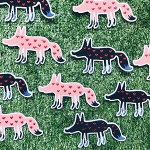 May include: A set of ten iron-on patches featuring foxes with hearts. The foxes are in black and pink with white accents. The hearts are red and black.