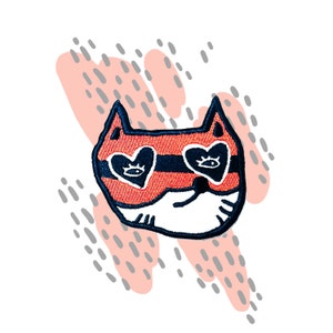 May include: A red and black embroidered iron-on patch of a cat wearing heart-shaped sunglasses. The cat has a white face and black whiskers.