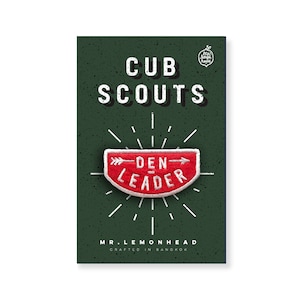 May include: Red and white embroidered patch with the text "Den Leader" and an arrow pointing to the right. The patch is on a green background with the text "Cub Scouts" and "Mr. Lemonhead Crafted in Bangkok".