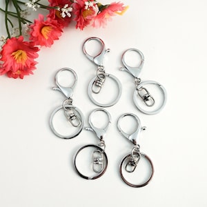 May include: Five silver keychains with a swivel clasp and a round ring. The keychains are on a white background.