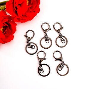 May include: Five black metal keychains with a swivel clasp and a round ring. The keychains are arranged in a semi-circle on a white background.