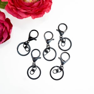 May include: Five black metal keychains with a swivel clasp and a round ring. The keychains are on a white background.