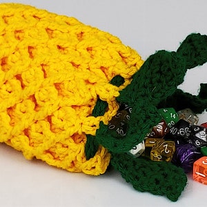May include: A yellow crocheted pineapple-shaped dice bag with green leaves and a wooden bead. The bag is open and spilling out colorful dice.