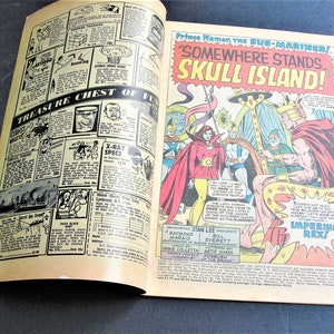 May include: A comic book cover featuring a red-haired superhero with a crown and a cape, standing on a throne. The text on the cover reads "Prince Namor the Sub-Mariner! "Somewhere Stands Skull Island!" Imperius Rex!"