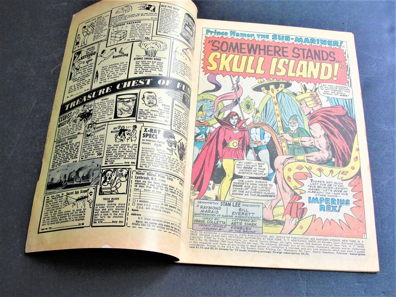 May include: A comic book cover featuring a red-haired superhero with a crown and a cape, standing on a throne. The text on the cover reads "Prince Namor the Sub-Mariner! "Somewhere Stands Skull Island!" Imperius Rex!"