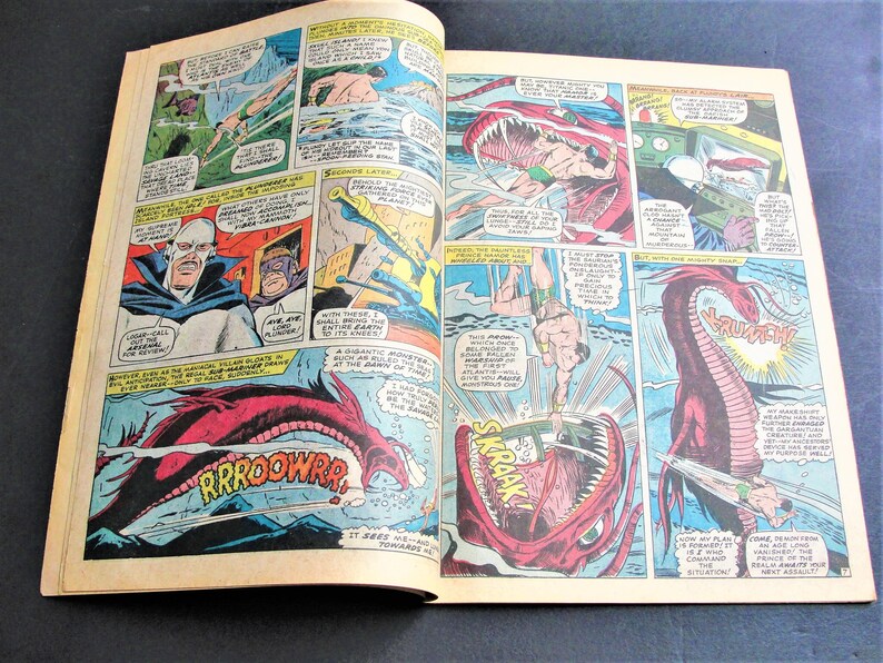 May include: A comic book page featuring a red and white monster with sharp teeth and a long tail. The monster is attacking a man in a blue and yellow costume. The text on the page reads "RROOWWR!" and "SKRAAK!"