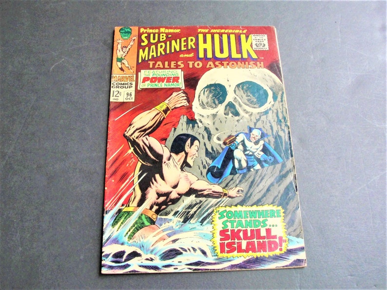 May include: A comic book cover featuring the Sub-Mariner and the Incredible Hulk. The cover is red, yellow, and blue with a skull image in the background. The text on the cover reads "Prince Namor, The Incredible Hulk, Sub-Mariner, Tales to Astonish, Featuring the Pounding Power of Prince Namor, Somewhere Stands... Skull Island!"