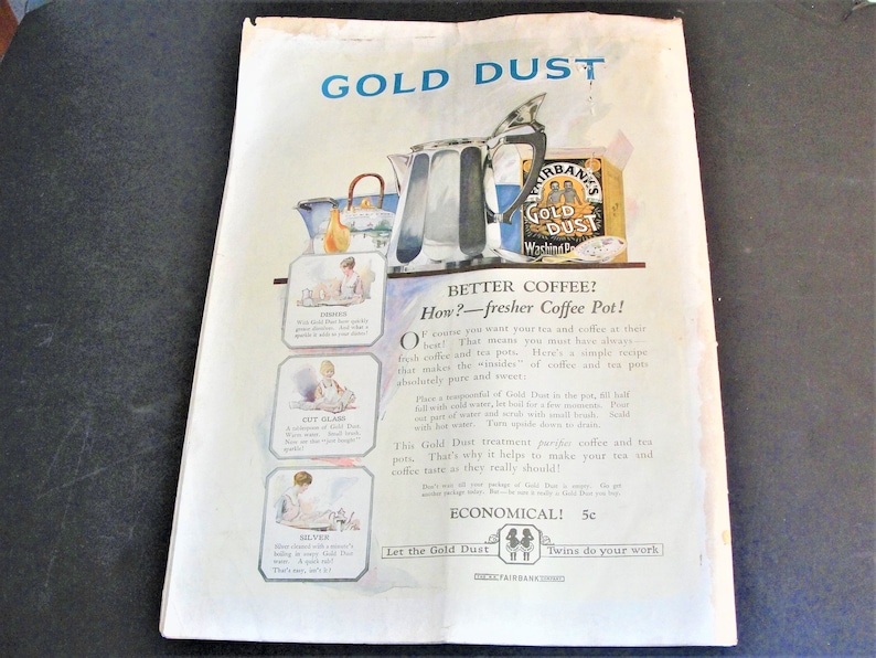 Op de afbeelding: Een vintage advertentie voor Gold Dust waspoeder, met een vrouw in een witte jurk die een koffiepot vasthoudt. De advertentie promoot het vermogen van het product om koffie en thee beter en schoner te laten smaken. De tekst luidt "Betere koffie? Hoe? - Een frissere koffiepot!" en "Laat de Gold Dust tweelingen het werk doen."