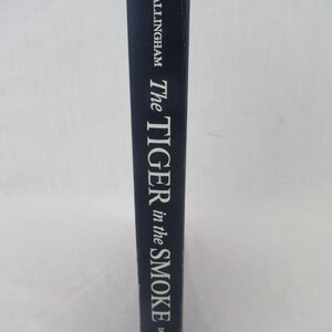 Puede incluir: Un libro de tapa dura de color azul marino con el título "The Tiger in the Smoke" del autor "Allingham" y la editorial "Doubleday" impresa en el lomo.