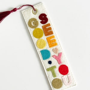 May include: A white felt bookmark with a red tassel. The bookmark has the word "GOODBYE" spelled out in colorful felt letters.