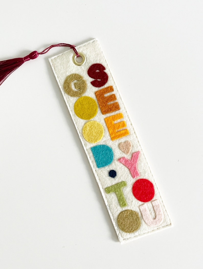 May include: A white felt bookmark with a red tassel. The bookmark has the word "GOODBYE" spelled out in colorful felt letters.
