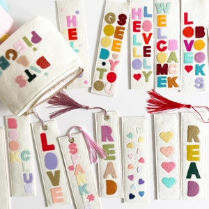 May include: A set of felt bookmarks with different words and designs. The words include "READ", "LOVE", "BOOK", "SPARK", "GO", "HELLO", "WELL", and "PIECE". The bookmarks are white with colorful felt letters and designs.