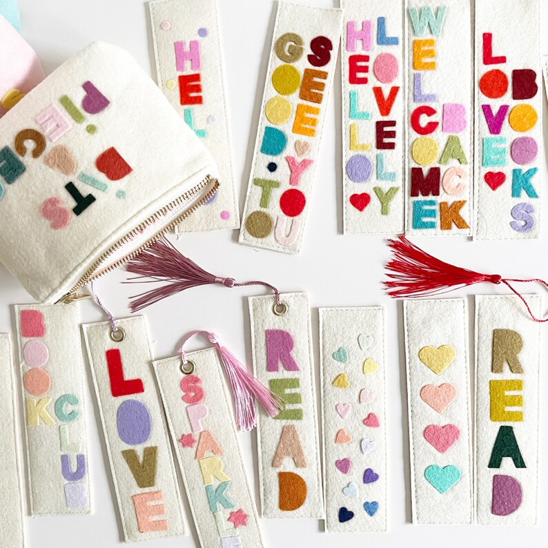 May include: A set of felt bookmarks with different words and designs. The words include "READ", "LOVE", "BOOK", "SPARK", "GO", "HELLO", "WELL", and "PIECE". The bookmarks are white with colorful felt letters and designs.