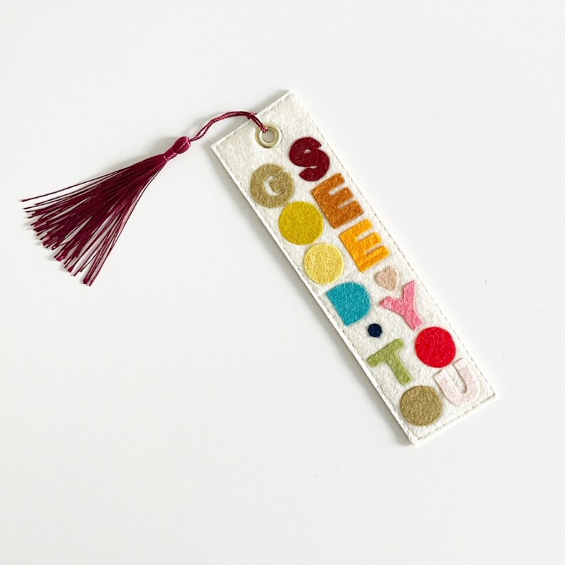 May include: A white felt bookmark with a red tassel. The bookmark has the words "See You" in rainbow colored felt letters.