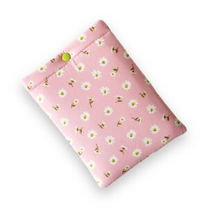 Può includere: Una custodia in tessuto rosa con un motivo a margherite. La custodia è rettangolare con angoli arrotondati e una chiusura con bottone verde. Le margherite sono bianche con centri gialli e steli verdi.