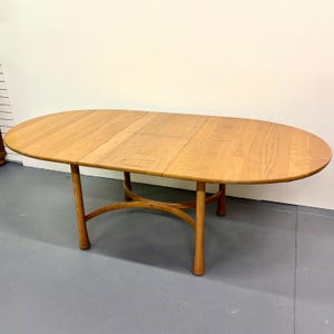 May include: Oval wooden dining table with a light brown finish. The table has a curved base and four legs. The table is approximately 72 inches long and 40 inches wide.