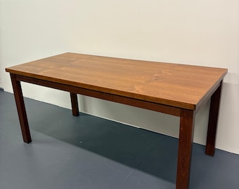 Puede incluir: Una mesa rectangular de madera con tapa marrón claro y patas marrón oscuro. La mesa mide aproximadamente 152 cm de largo, 76 cm de ancho y 76 cm de alto. La mesa tiene un diseño simple y minimalista.