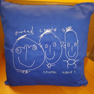Peut inclure: Un coussin bleu avec des dessins brod&eacute;s blancs de trois visages. Les visages sont &eacute;tiquet&eacute;s "Grandad", "Charlie" et "Charlie Aged 5".