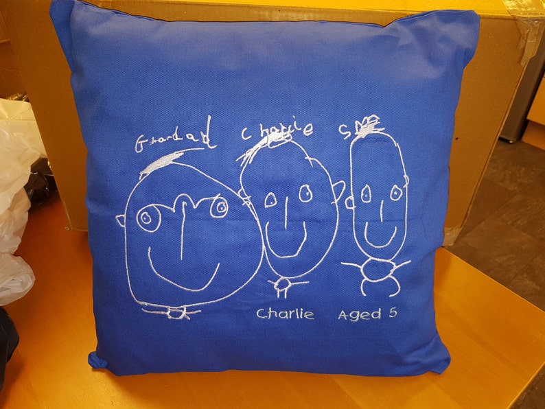 Peut inclure: Un coussin bleu avec des dessins brod&eacute;s blancs de trois visages. Les visages sont &eacute;tiquet&eacute;s "Grandad", "Charlie" et "Charlie Aged 5".