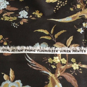 May include: Close-up of brown fabric with a floral pattern featuring birds, leaves, and flowers in shades of blue, green, and yellow. The fabric has a fringed edge and a white label that reads "Total Action Fabric Flourdizer Screen Printed".