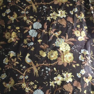 May include: A dark brown fabric with a repeating pattern of stylized birds, flowers, and leaves. The flowers are in shades of yellow and white, and the leaves are in shades of brown and green.