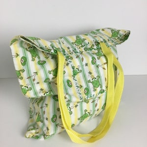 May include: A yellow and green striped tote bag with a frog pattern. The bag has two yellow straps.