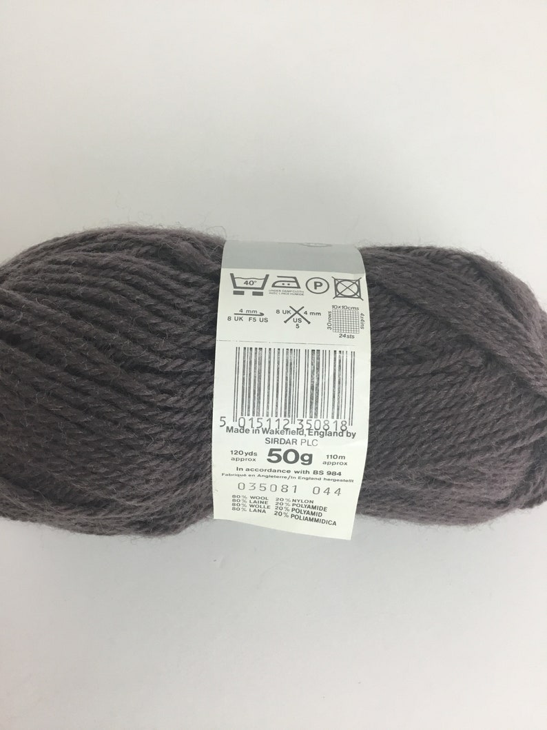May include: A ball of dark gray yarn with a label that reads "5 015112 350818 Made in Wakefield, England by SIRDAR PLC 120yds 50g 110m approx approx In accordance with BS 984 035081 044 80% WOOL 20% NYLON 80% LAINE 20% POLYAMIDE 80% WOLLE 20% POLYAMID 80% LANA 20% POLIAMMIDICA"