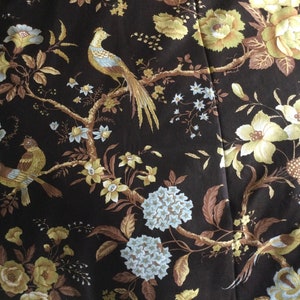 May include: A brown fabric with a floral pattern featuring yellow and white flowers, brown leaves, and birds. The birds are brown, yellow, and blue.