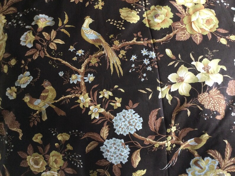 May include: A brown fabric with a floral pattern featuring yellow and white flowers, brown leaves, and birds. The birds are brown, yellow, and blue.