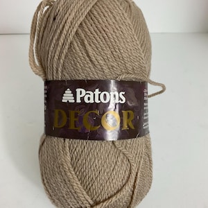 May include: A ball of Patons Decor yarn in a neutral tan color. The yarn is tightly wound and wrapped with a brown label featuring the brand name and product details. Ideal for knitting and crochet projects.