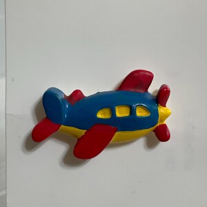 May include: A colorful toy airplane with a blue fuselage, red wings and propeller, and yellow accents. The toy plane has three yellow windows and is designed for children.