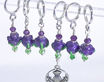 May include: Set of five purple and green thistle flower stitch markers with a silver charm of a thistle. The stitch markers are attached to silver rings.