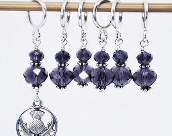 May include: Set of six purple crystal stitch markers with silver rings and a silver charm featuring a stylized thistle.