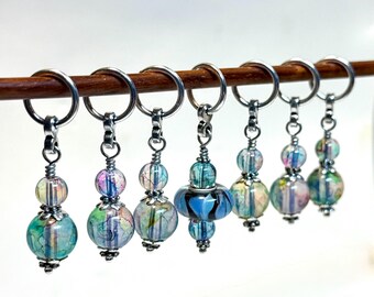 Opal glass bead stitch markers with large lampwork BOR marker. Mixed shades of lavender, blue, green. Optional Sari Silk gift bag.