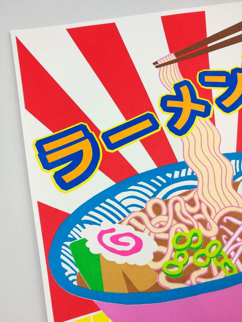 Pu&ograve; includere: Un'illustrazione colorata di una ciotola di ramen con bacchette. La ciotola &egrave; rosa con un bordo blu e un motivo bianco e blu. I noodles sono gialli e bianchi, e c'&egrave; un vortice rosa in cima. Il testo "ラーメン" &egrave; scritto in caratteri giapponesi.