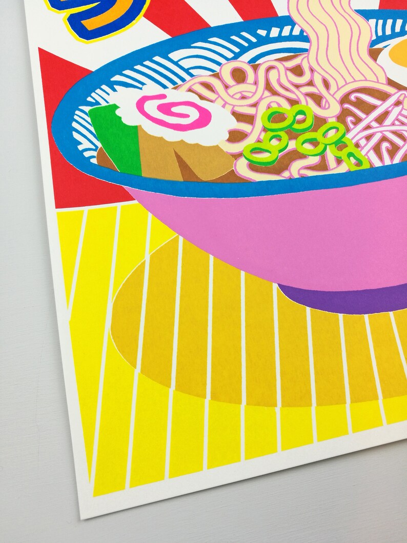 Pu&ograve; includere: Una ciotola rosa di ramen con noodles, cipolle verdi, una torta di pesce rosa e bianca e un uovo marrone. La ciotola &egrave; su una superficie a strisce gialle e bianche.