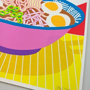 Pu&ograve; includere: Una ciotola rosa di ramen con noodles, cipolle verdi e due uova. La ciotola &egrave; su una superficie a strisce gialle e bianche. L'immagine &egrave; firmata "SMW 2019".