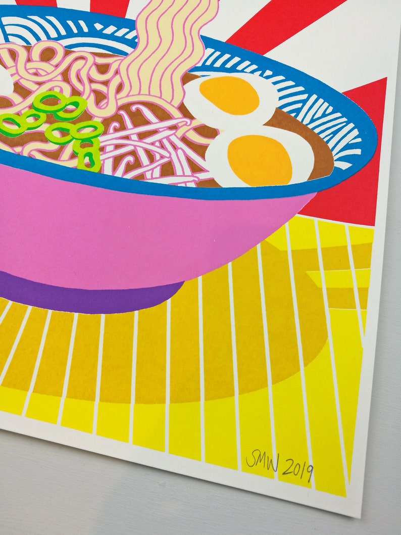 Pu&ograve; includere: Una ciotola rosa di ramen con noodles, cipolle verdi e due uova. La ciotola &egrave; su una superficie a strisce gialle e bianche. L'immagine &egrave; firmata "SMW 2019".