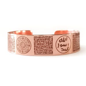 Puede incluir: Una pulsera de brazalete de color cobre con intrincados diseños grabados. La pulsera presenta patrones geométricos, motivos circulares y caligrafía árabe. El diseño de brazalete abierto permite un fácil uso. La pulsera mide aproximadamente 6,35 cm de ancho.