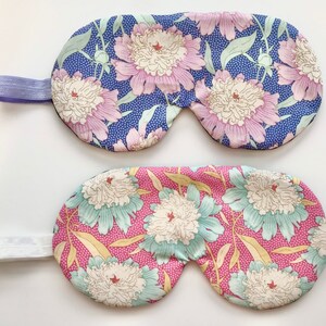 May include: Two floral sleep masks. One features a blue background with white polka dots and large pink and white flowers. The other has a pink background with white polka dots and teal and white flowers. Both have elasticated bands.