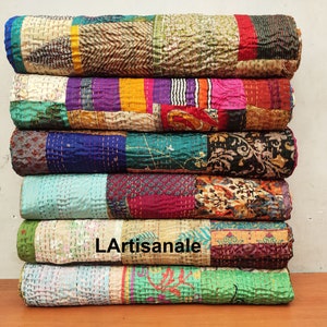 May include: A stack of colorful kantha quilts made from recycled saris. The quilts are layered in a variety of patterns and colors, including blue, green, purple, pink, and yellow. The quilts are hand-stitched and have a unique, vintage look.