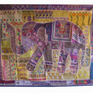 Op de afbeelding: Een kleurrijk patchwork wandkleed met een groot olifantendesign. De olifant is gemaakt van verschillende stoffen in tinten paars, geel, roze en bruin. Het wandkleed heeft een blauwe rand.