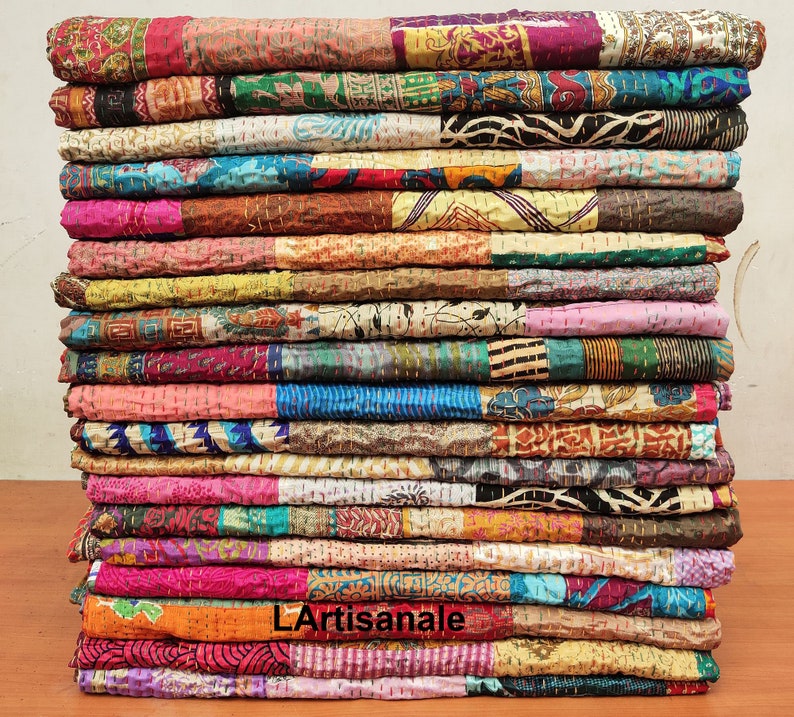 May include: A stack of colorful kantha quilts made from recycled saris. The quilts are layered in a variety of patterns and colors, including pink, blue, green, yellow, and orange. The quilts are hand-stitched and have a unique, vintage look.