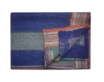 May include: A folded blue and multi-colored patchwork quilt. The quilt features a variety of textures and patterns, including stripes and squares. The color palette includes shades of blue, gray, orange, and pink.